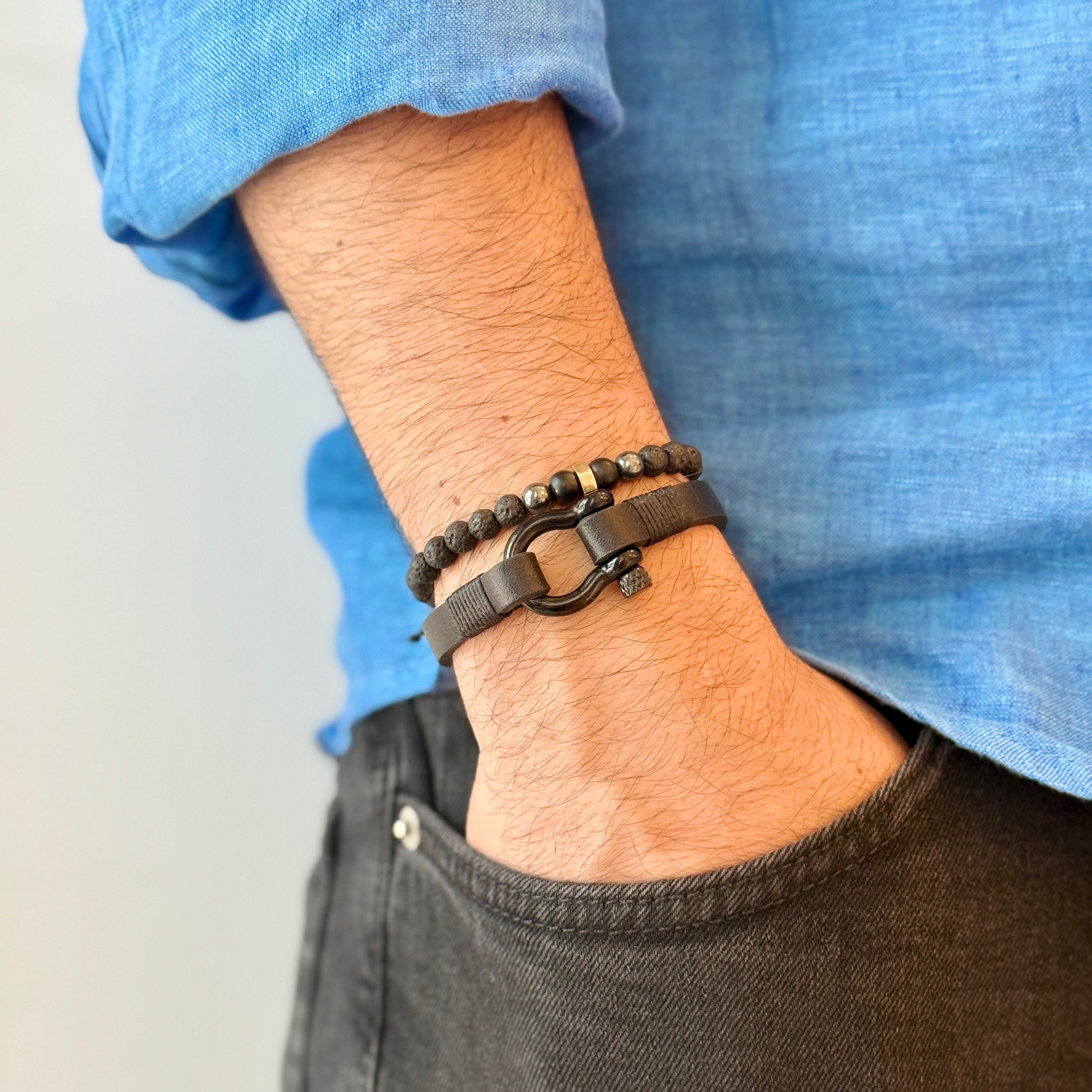 Person wearing a bracelet on a wrist with a blue shirt and dark pants.