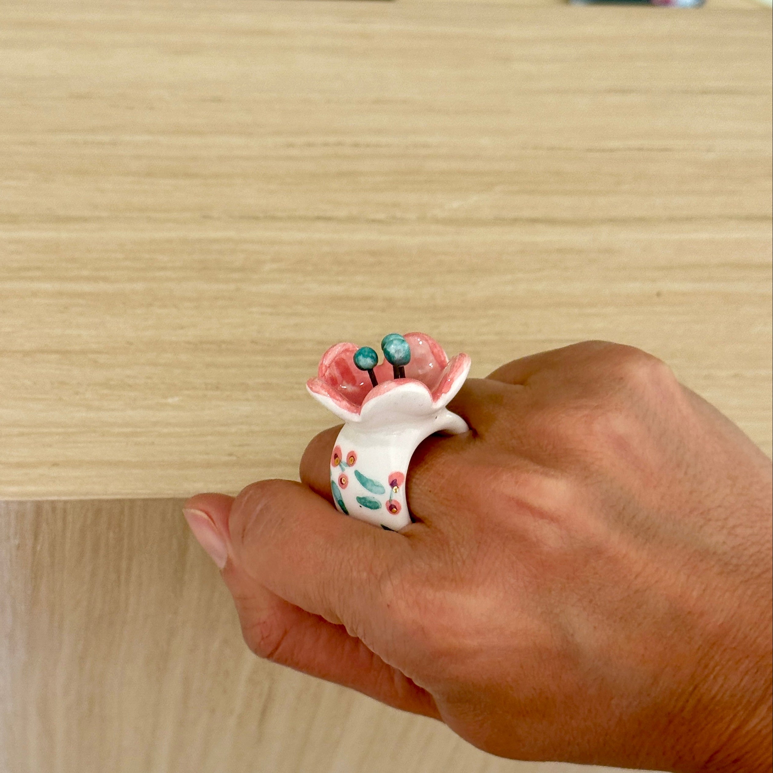 Hand wearing a decorative ring with floral design and small beads on a wooden surface