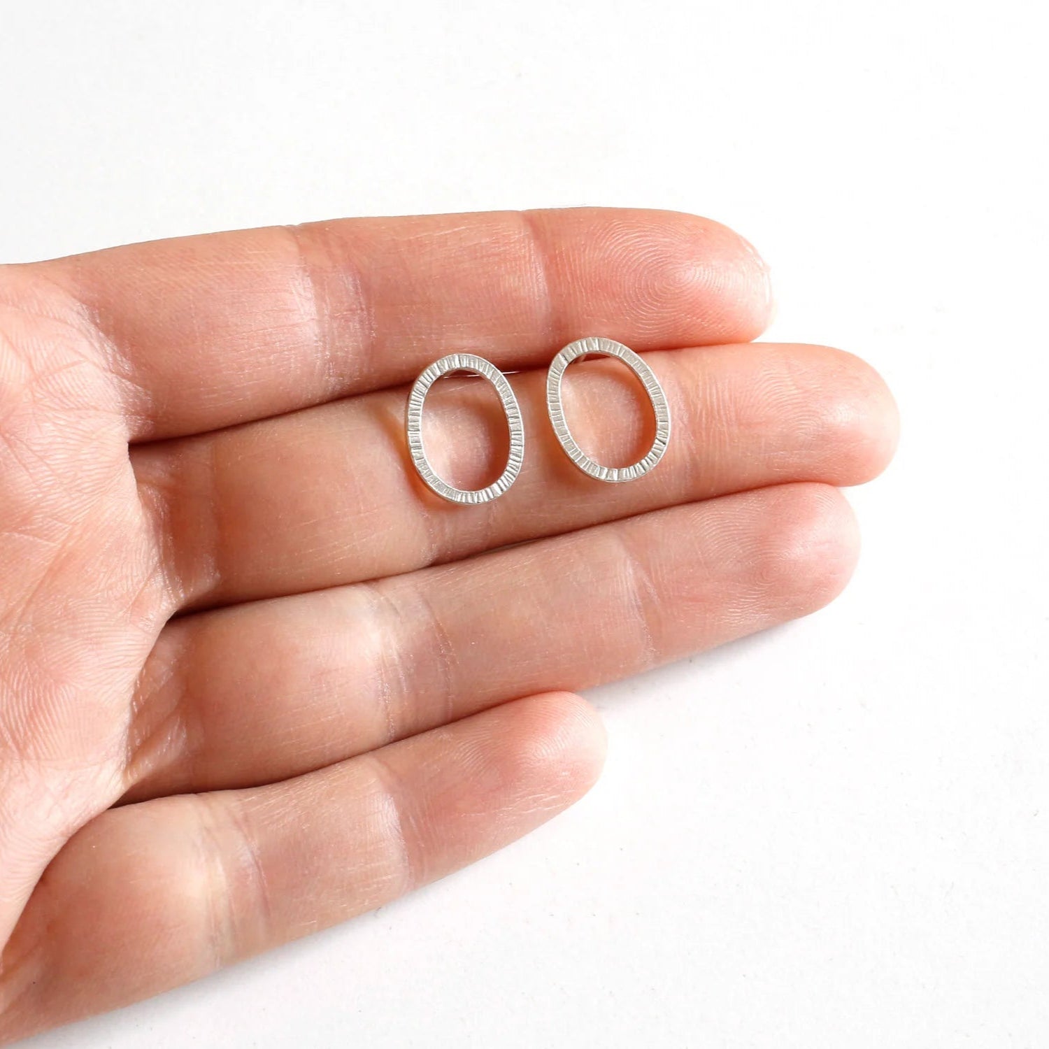 Silver hoop earrings held between fingers on a white background