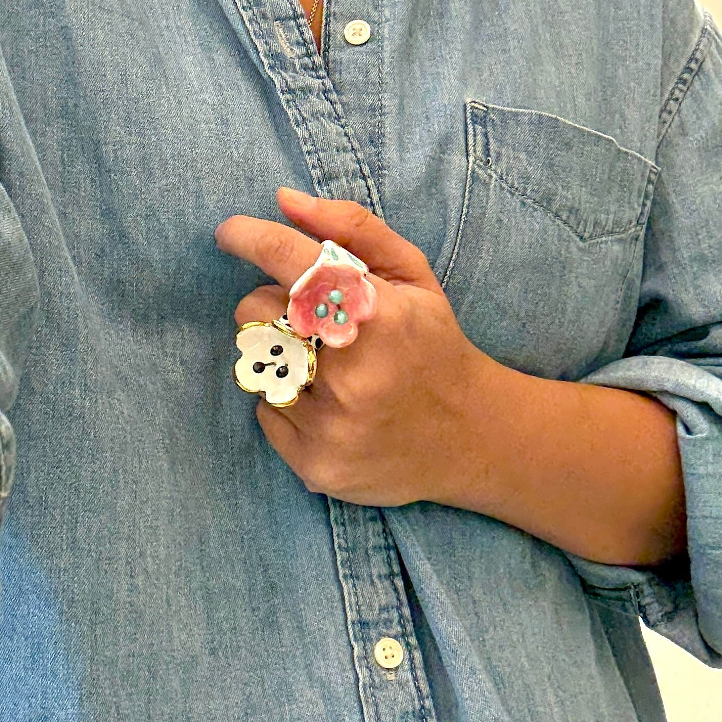 Hand wearing a pink flower-shaped ring with a blue denim shirt background