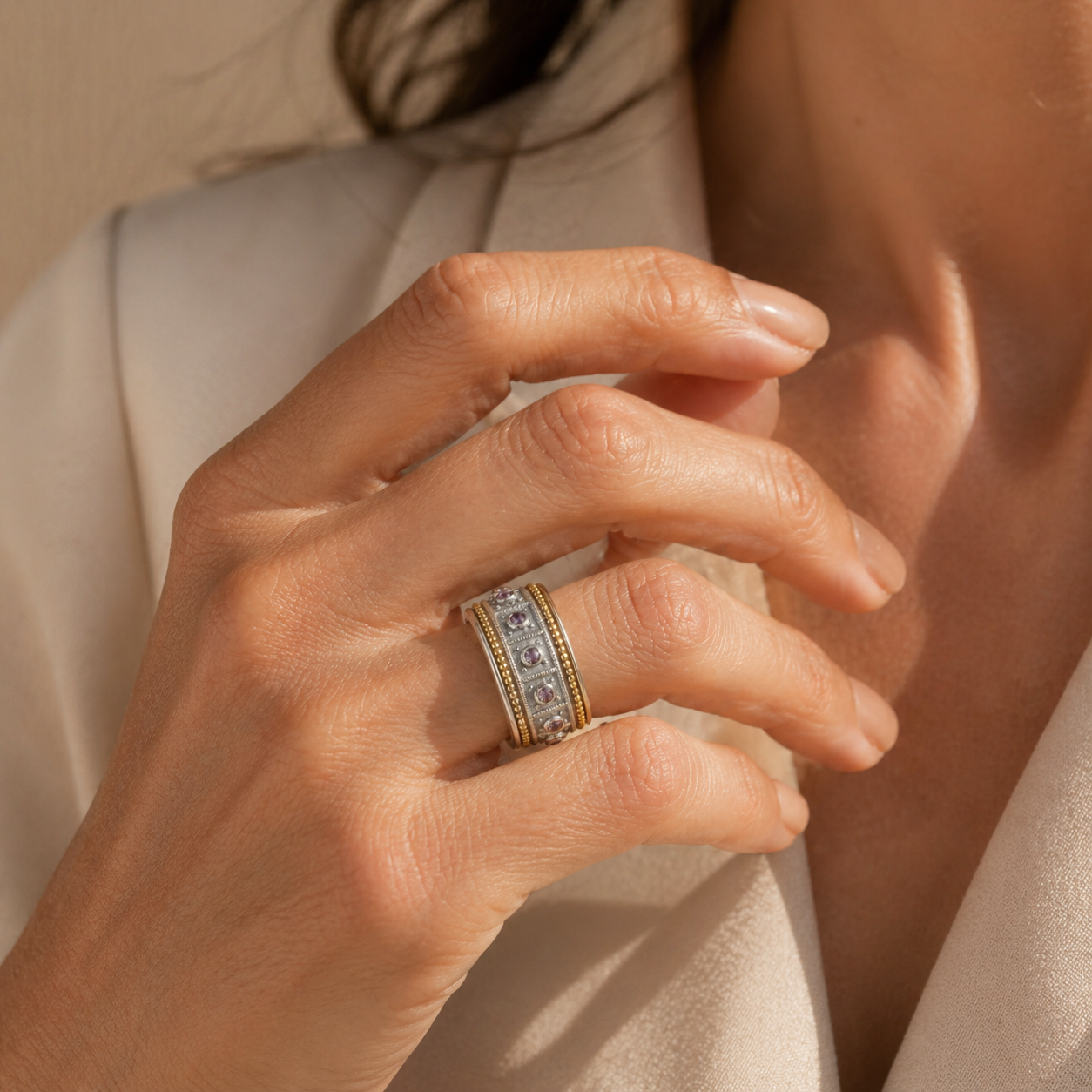 Close-up of a hand wearing a gold ring with gemstones against a neutral background