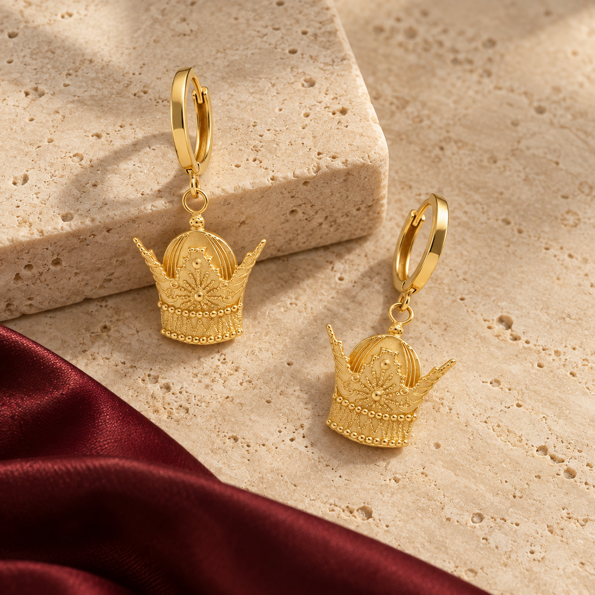 Royal Crown Drop Earrings staged on travertine and burgundy silk